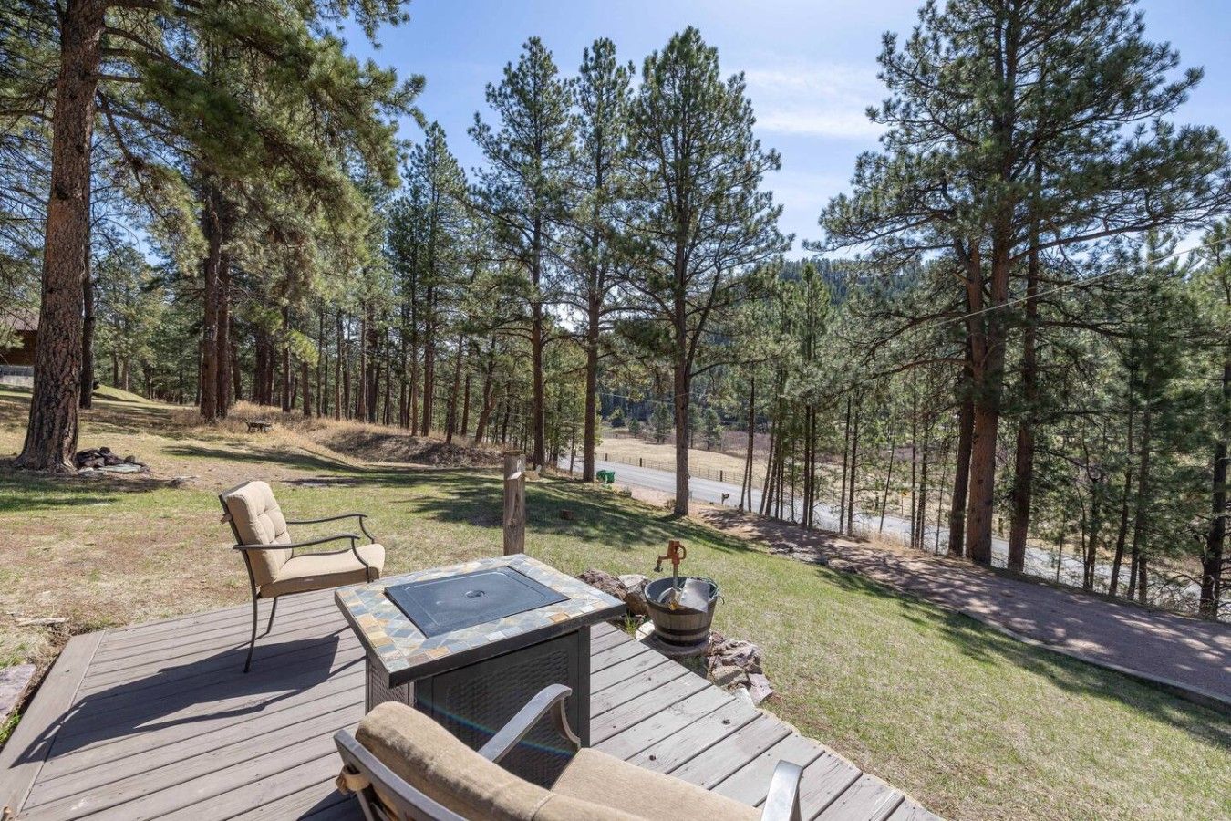 A deck with outdoor furniture, a fire pit, and a view of a forested area.