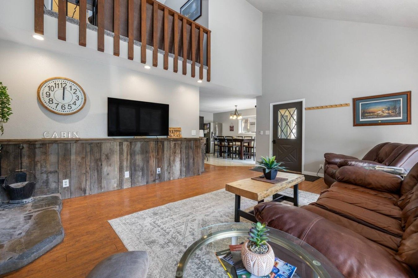 A modern living room with a wooden bench, a leather sofa, a glass coffee table, and a TV mounted on a wooden wall.