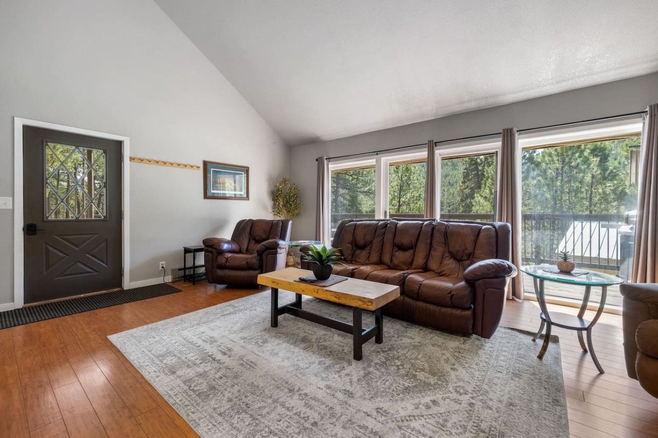 A living room with a brown leather sofa, two armchairs, a coffee table, and a glass table with a plant.
