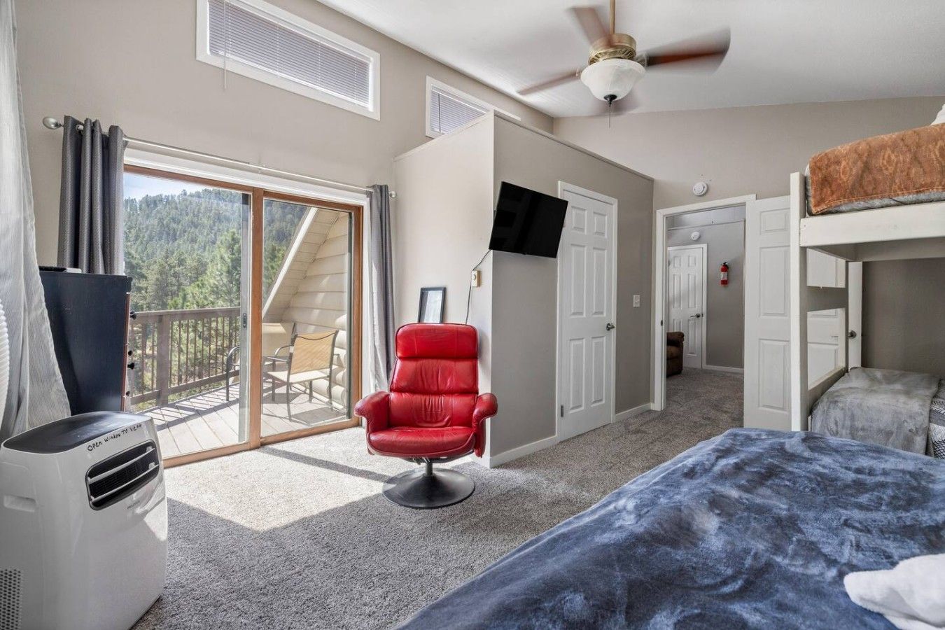 Un dormitorio con cama, una silla roja, un televisor y un balcón con una silla.