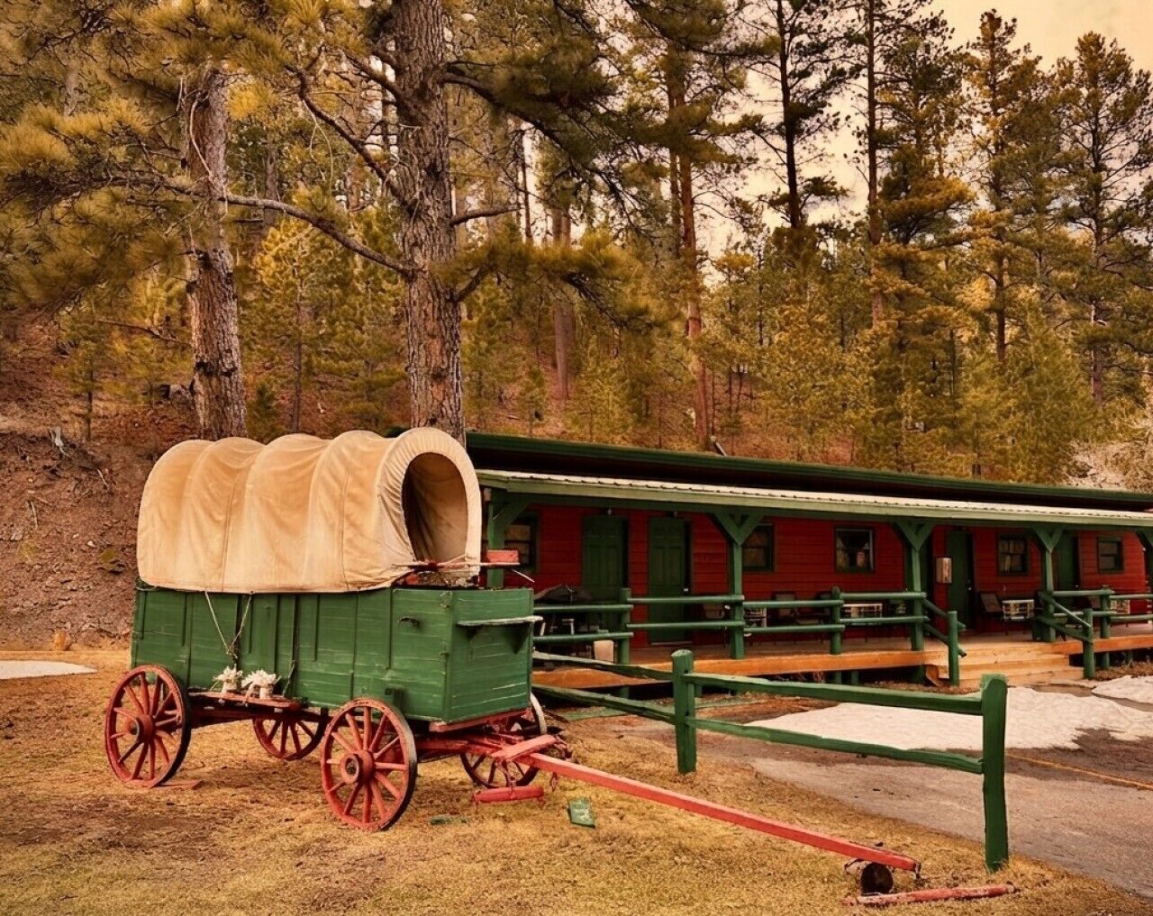A covered wagon parked in front of a red building with green railings and benches.
