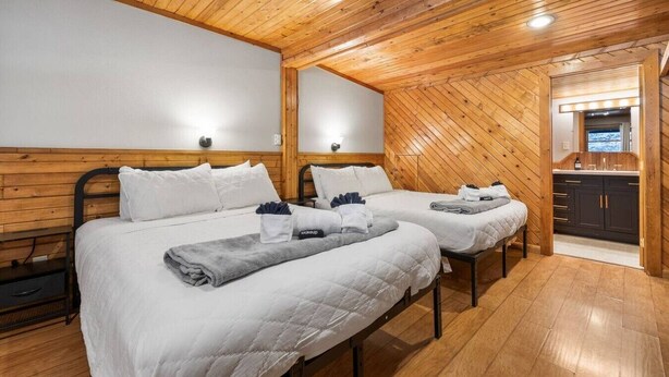 A room with two beds, wooden walls, a small kitchenette, and a ceiling light. - Room 17 – Queen Beds (Lead)