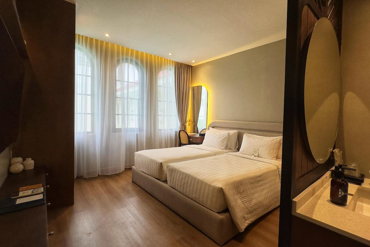 Une chambre d’hôtel avec deux lits, un grand miroir, une table de chevet avec une bouteille et un petit bureau avec une chaise.