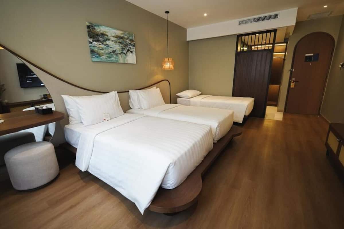 Une chambre d’hôtel avec deux lits, un bureau, une chaise, un petit pouf, un tableau au mur et une porte équipée d’un système de sécurité.