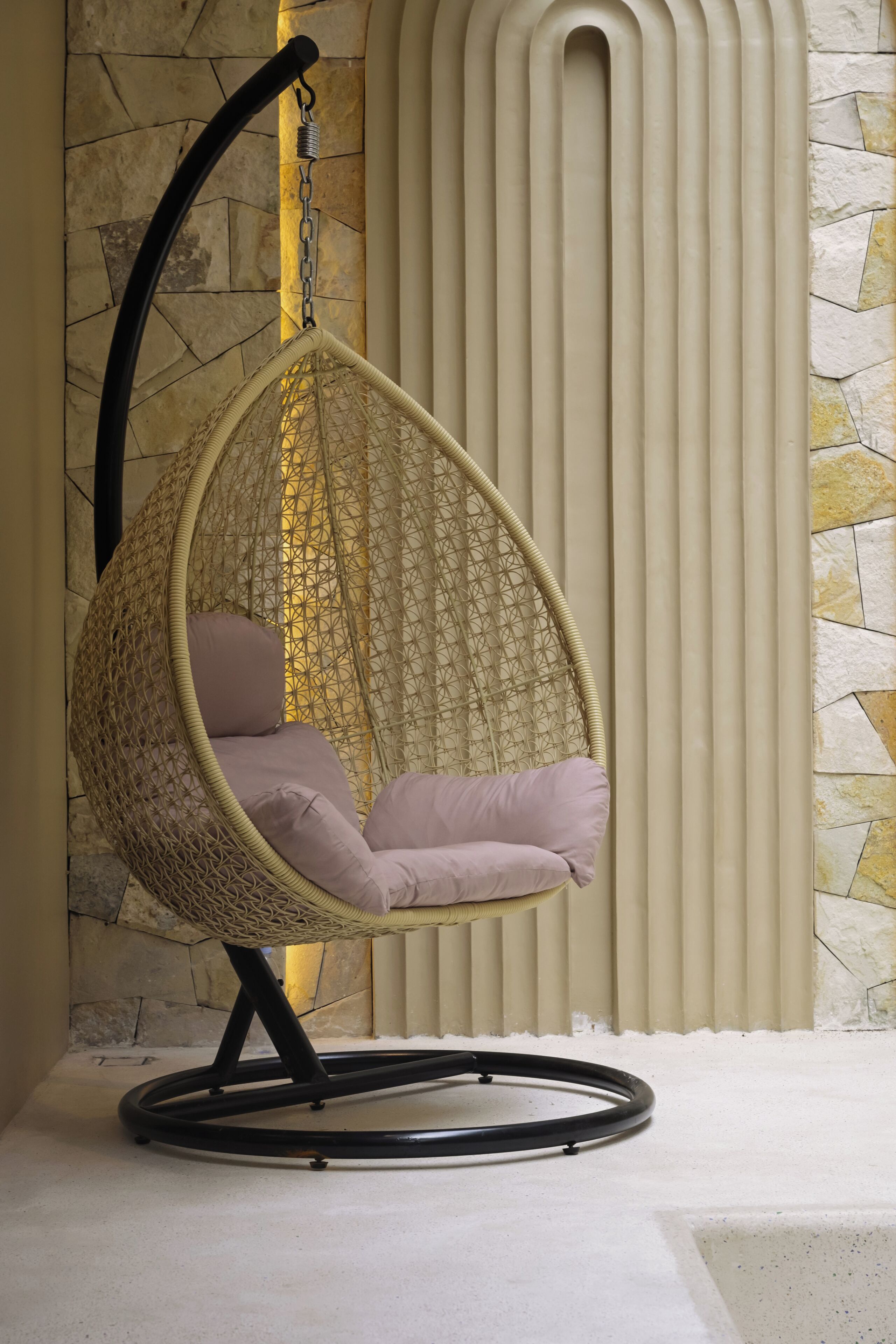 A hanging egg chair with cushions, a stone wall, and a radiator.