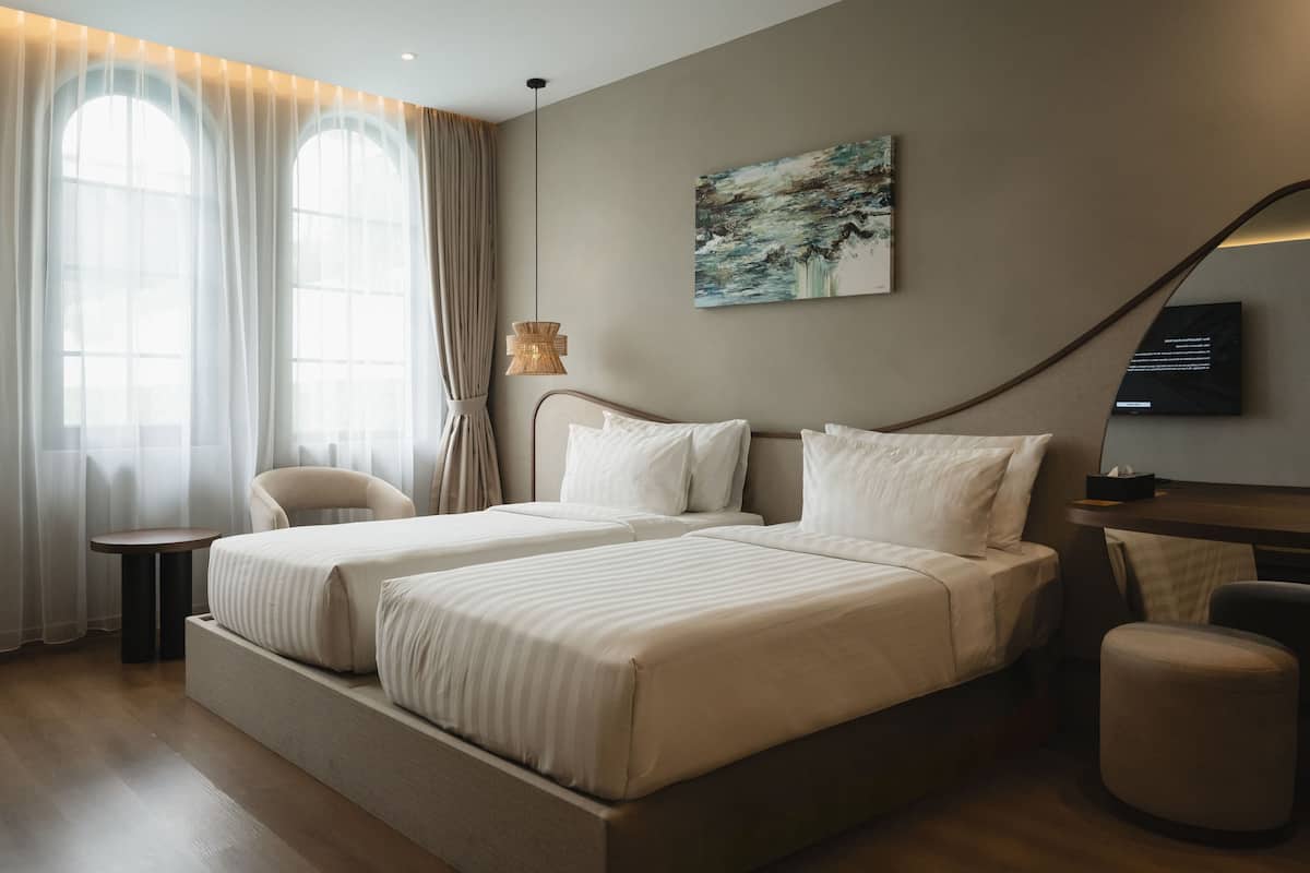 Une chambre d’hôtel avec deux lits, un bureau, une chaise, une télévision et un tableau au mur.