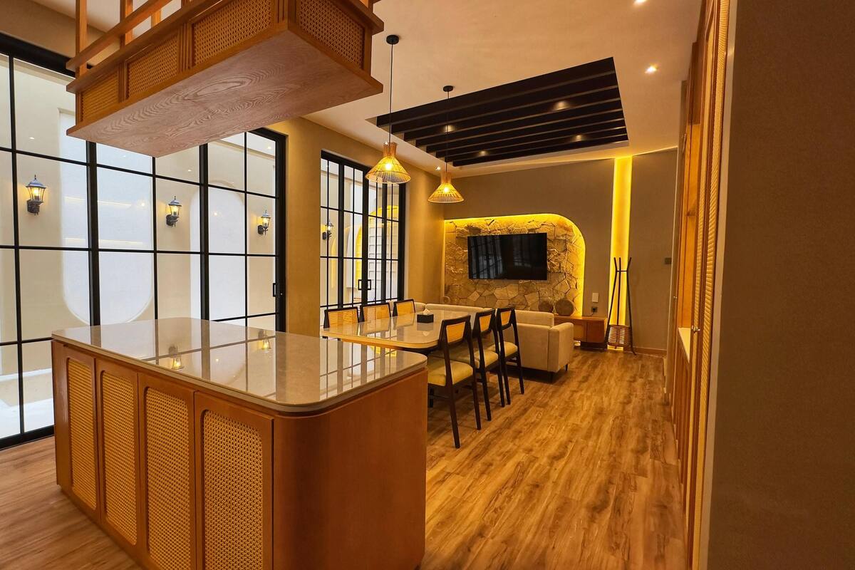 Un intérieur moderne avec un îlot central, un coin salon et un téléviseur fixé à un mur en pierre.