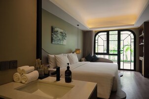 Une chambre d’hôtel dotée d’un grand lit, d’une table de chevet avec des articles de toilette, d’une vue sur la verdure par la fenêtre et d’un design moderne.