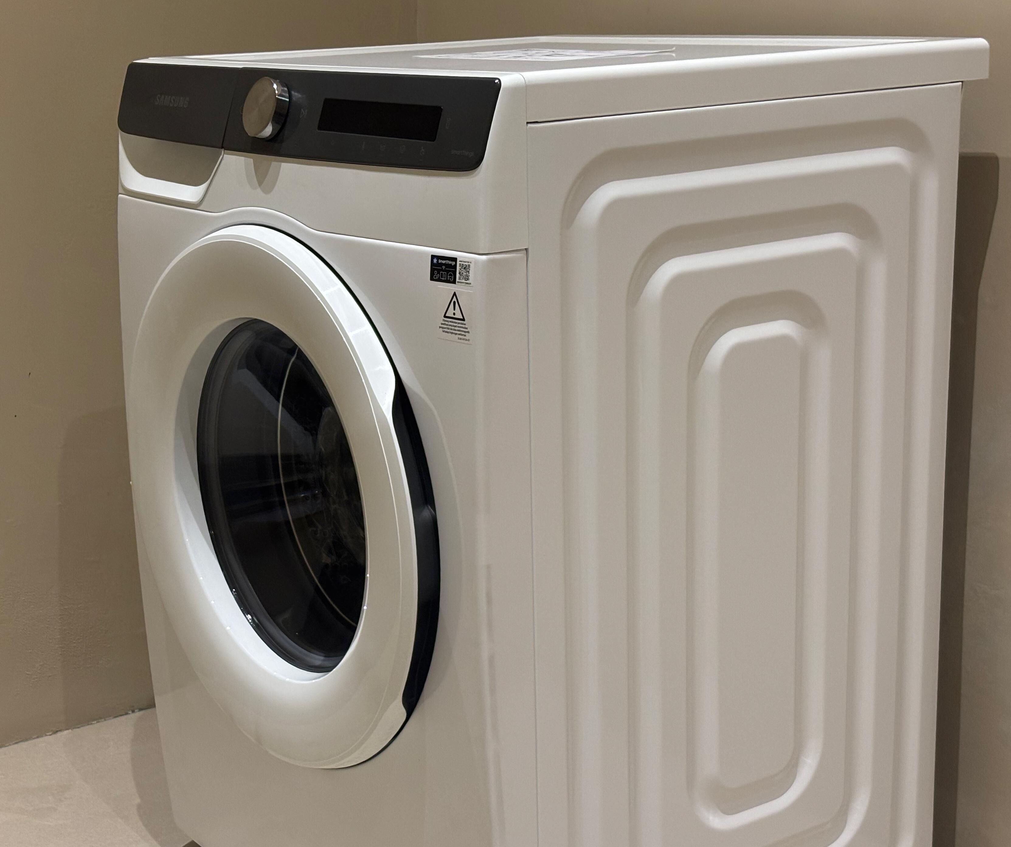 A white front-loading washing machine with a control panel and a safety warning label.