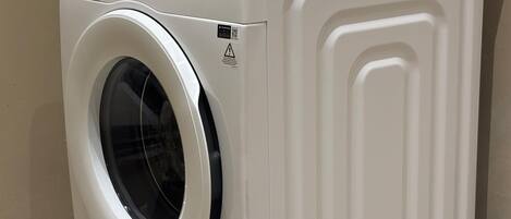 A white front-loading washing machine with a control panel and a safety warning label.