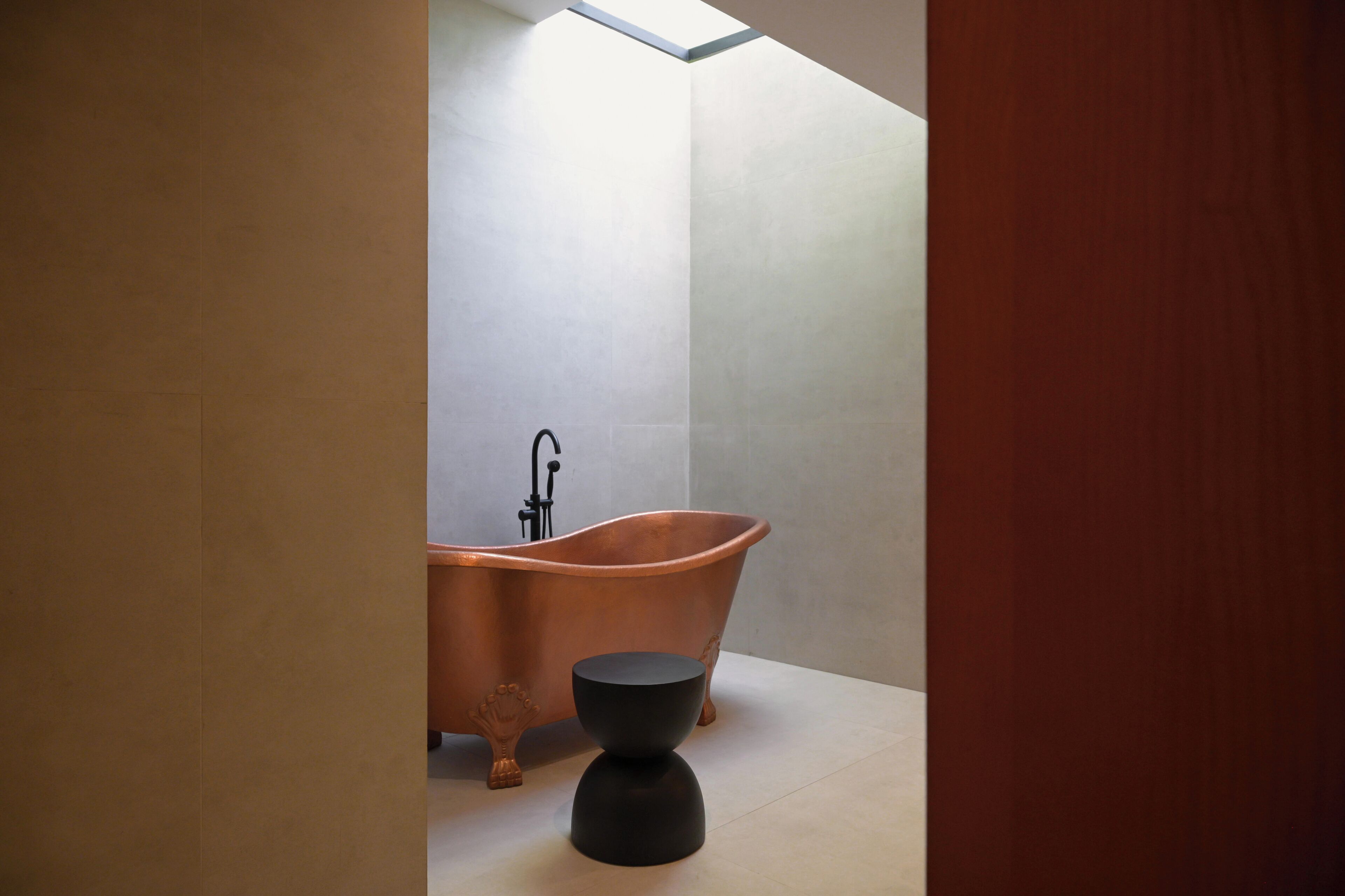 A modern bathroom with a freestanding copper bathtub, a black pedestal sink, and a skylight above.