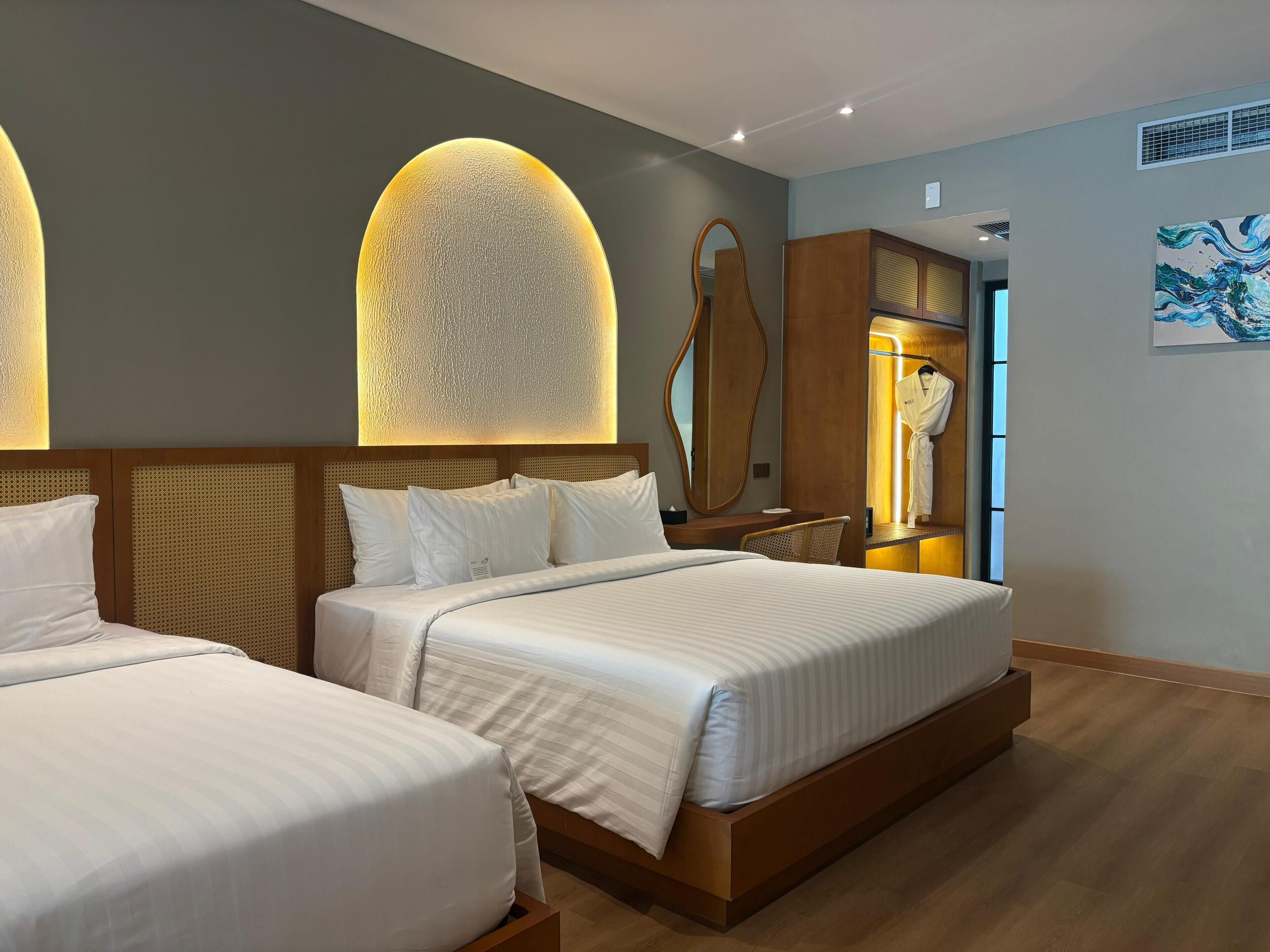 Ein Hotelzimmer mit zwei Betten, einem großen Spiegel, einem Kleiderhaken mit einem Bademantel und einem Gemälde an der Wand.