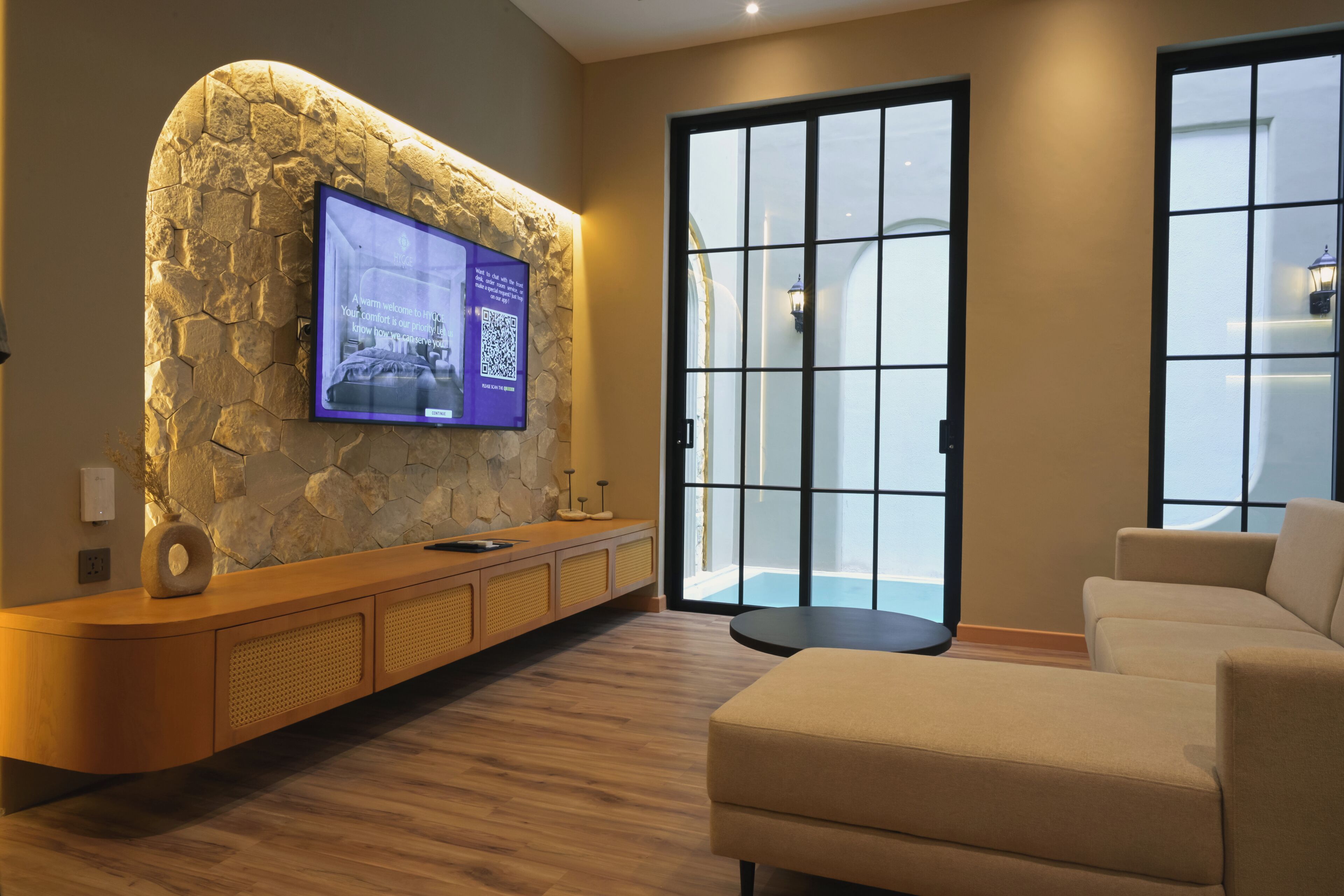 A modern lobby with a stone wall, a flat-screen TV, a wooden reception desk, a sofa, and a large glass door.