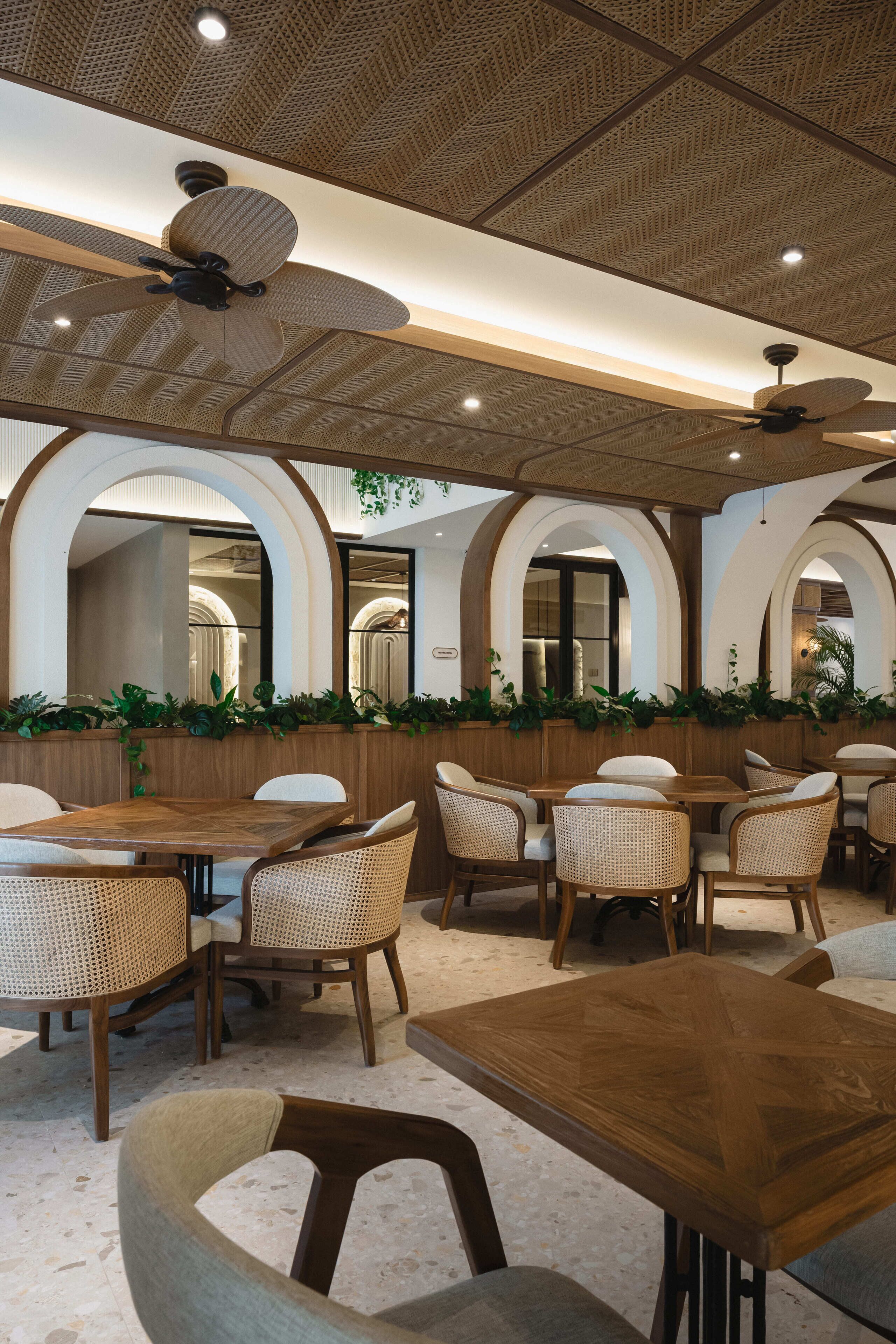 A restaurant with wooden tables and chairs, ceiling fans, and arched windows.