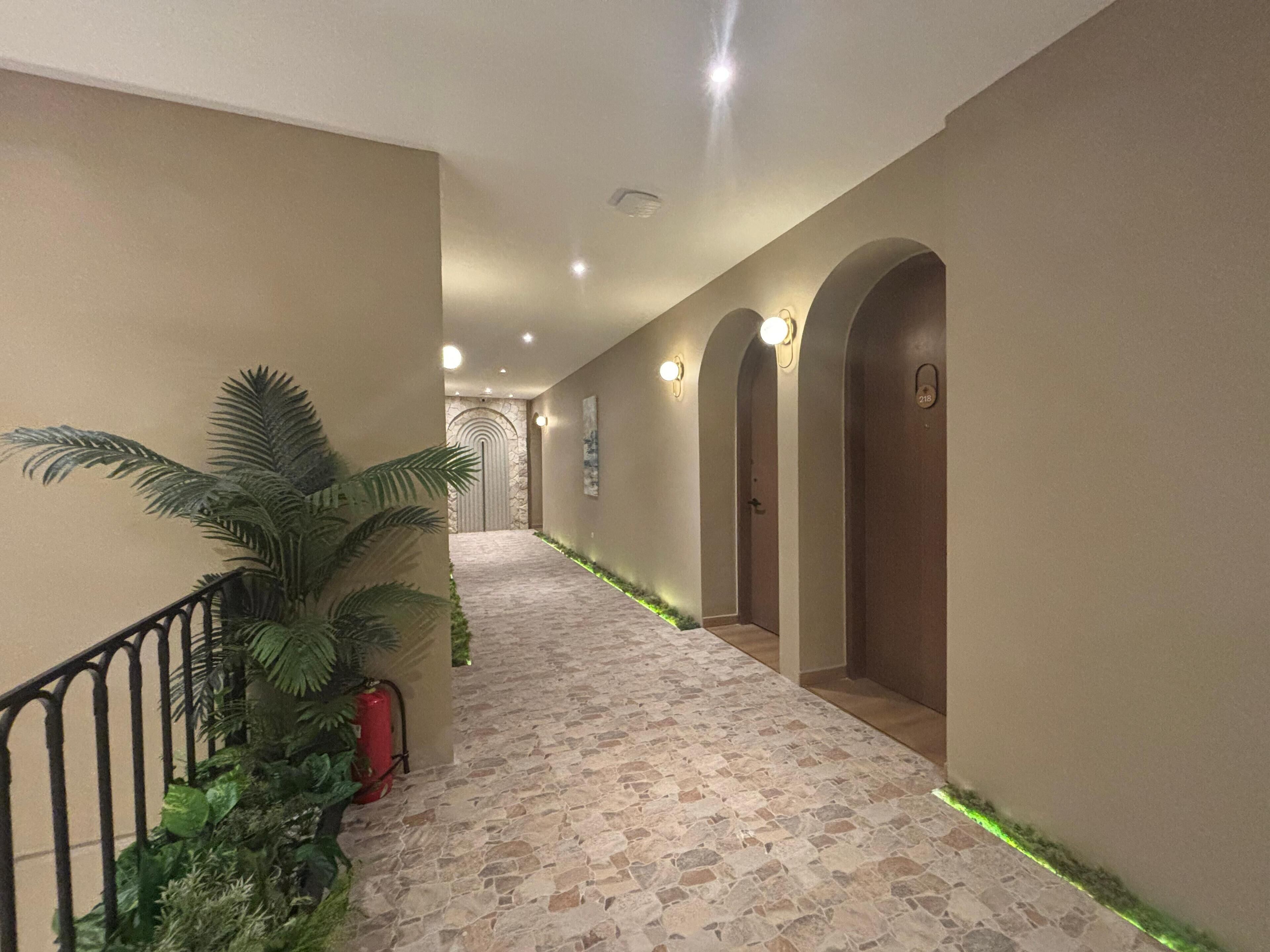A hallway with a stone floor, potted plants, and doors with numbers.