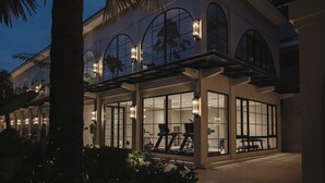 Ein modernes Gebäude mit großen Fenstern, Außenbereich mit Sitzgelegenheiten und einem überdachten Bereich mit Fitnessgeräten.