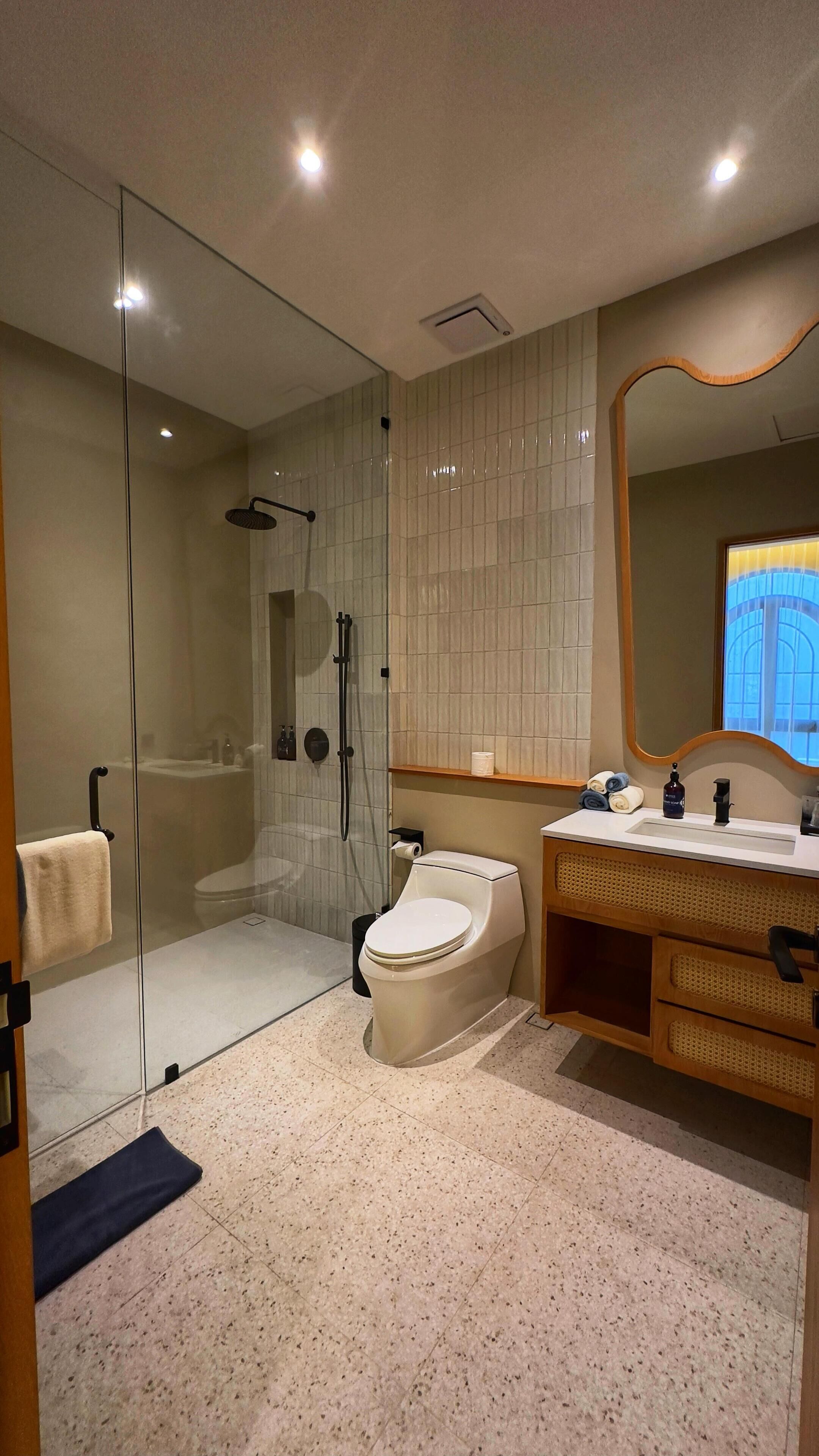 Een moderne badkamer met een douchecabine van glas, een toilet en een wastafel met spiegel.