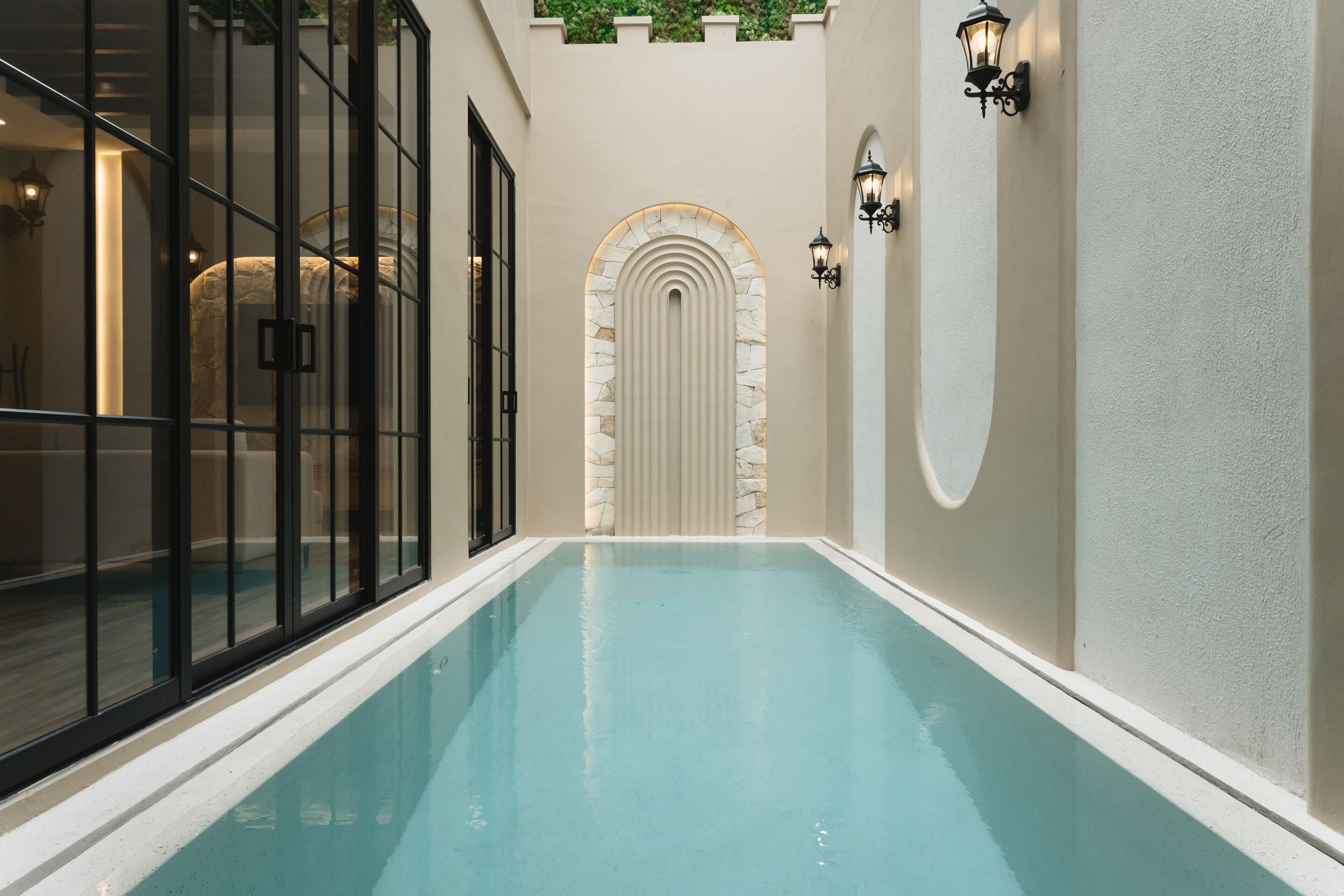 A swimming pool with a stone archway, glass doors, and wall-mounted lights.