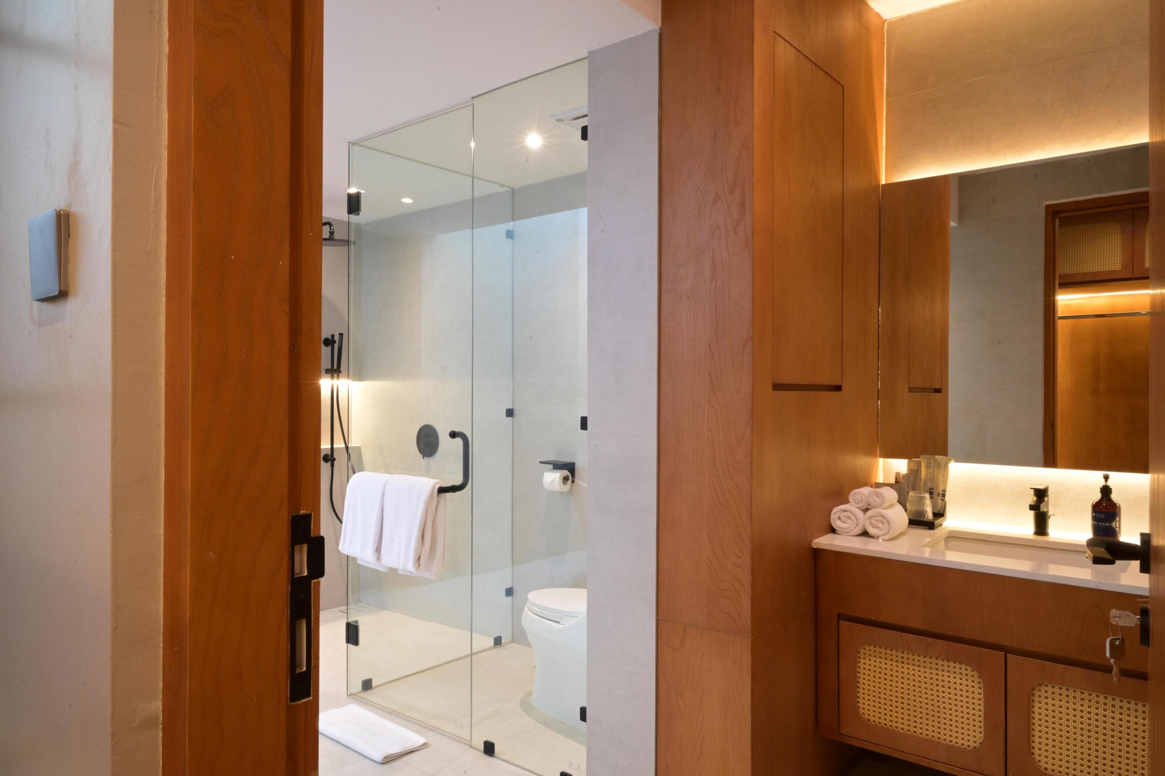 A modern bathroom with a glass-enclosed shower, a wooden vanity with a mirror, and a toilet.