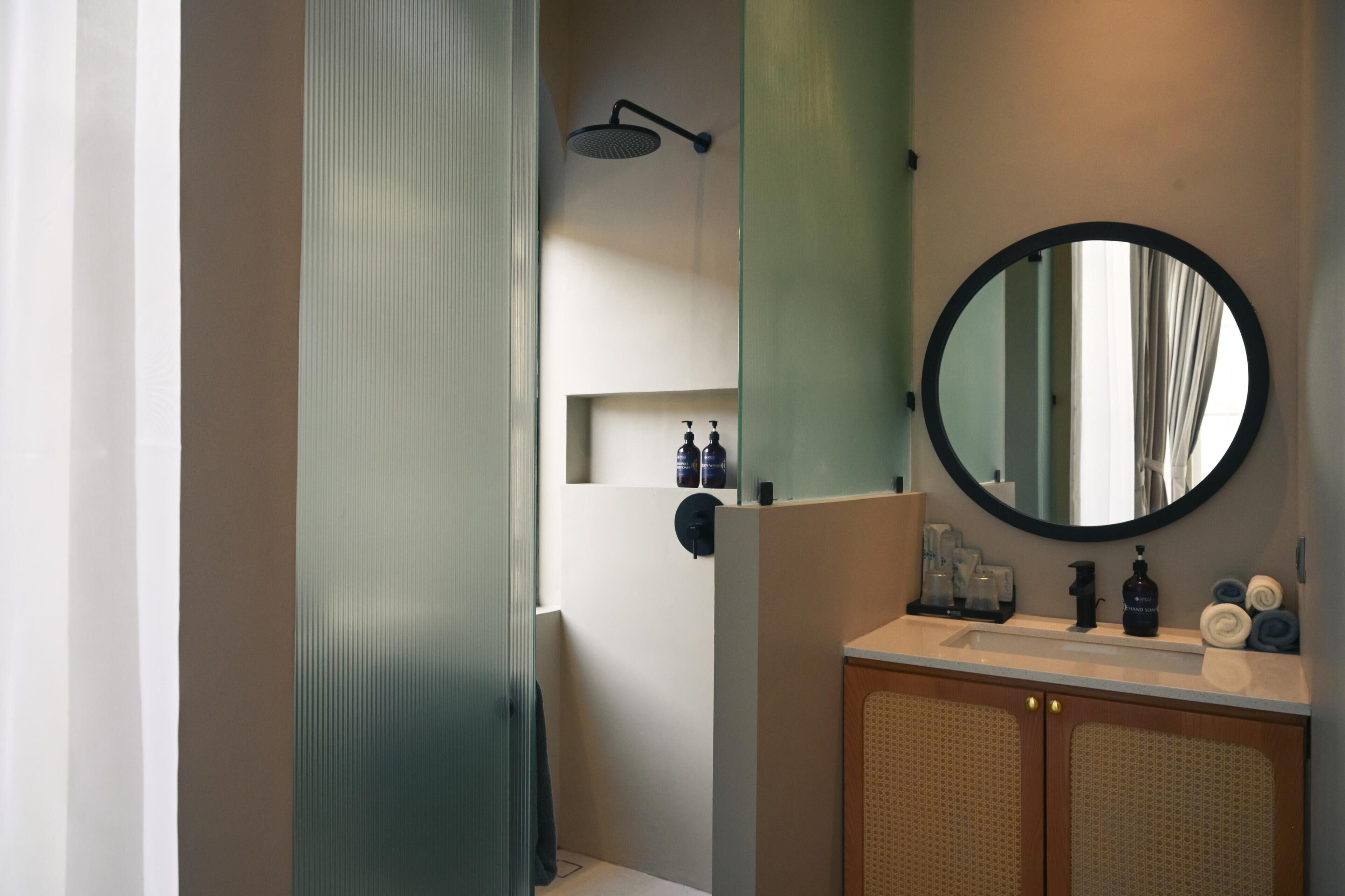 Une salle de bain avec une douche, un miroir rond et un lavabo équipé de produits de toilette.