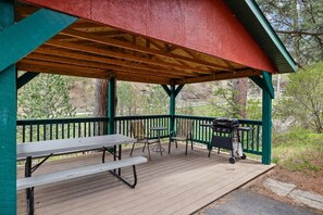 A covered outdoor seating area with a picnic table and chairs, a grill, and a view of the surrounding forest. - Room 20 – Spacious Stay (Lead)