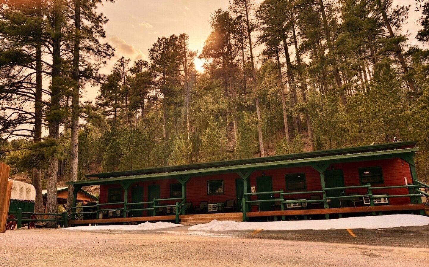 A red building with green trim, surrounded by tall trees and snow on the ground.