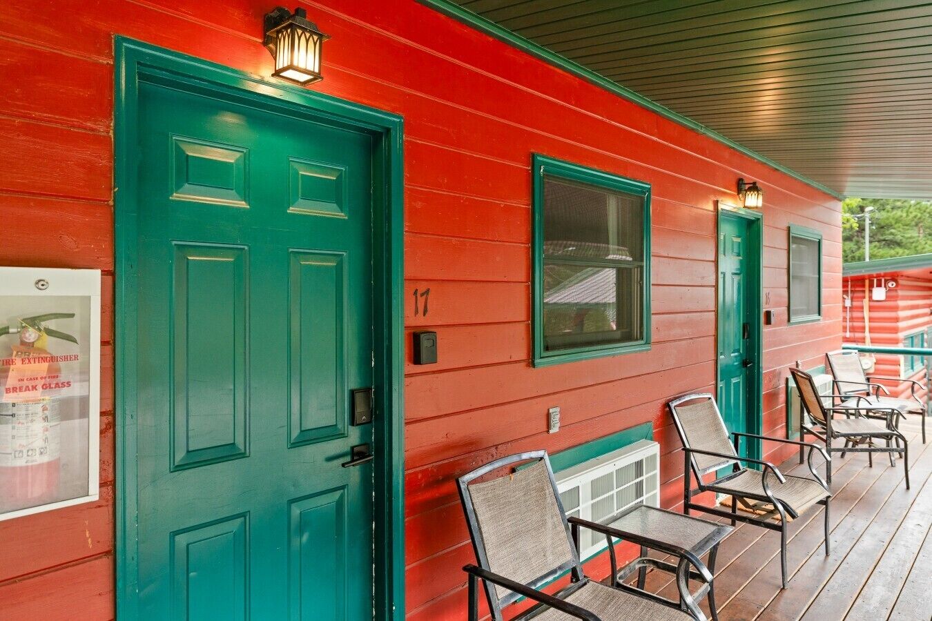 A red building with green doors and windows, numbered 17, and a porch with metal chairs.