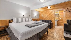 Une chambre d’hôtel moderne équipée d’un lit, de tables de chevet, d’un canapé, d’une télévision et d’un mur en bois.