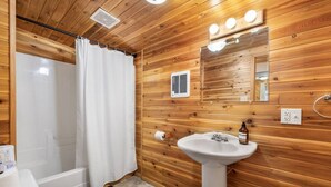Une salle de bain aux murs lambrissés, équipée d’une douche, de toilettes, d’un lavabo et d’un miroir.