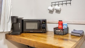 A kitchen area with a coffee maker, microwave, and a coffee cup holder on the wall.
