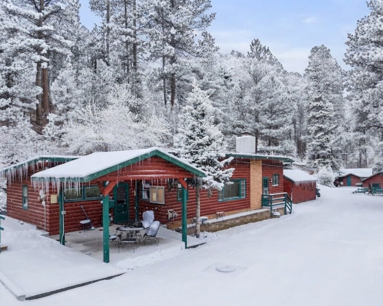 Une cabane en rondins dotée d’un porche abrité, d’un petit coin repas et offrant une vue sur une forêt enneigée.