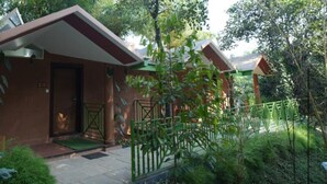 A small, single-story building with a flat roof and a door, surrounded by lush greenery and a metal fence. - Holiday Courtyard (Vythiri)