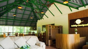 A reception area with a wooden reception desk, a beige sofa, and a sign that reads "Holiday Courtyard." - Holiday Courtyard (Vythiri)