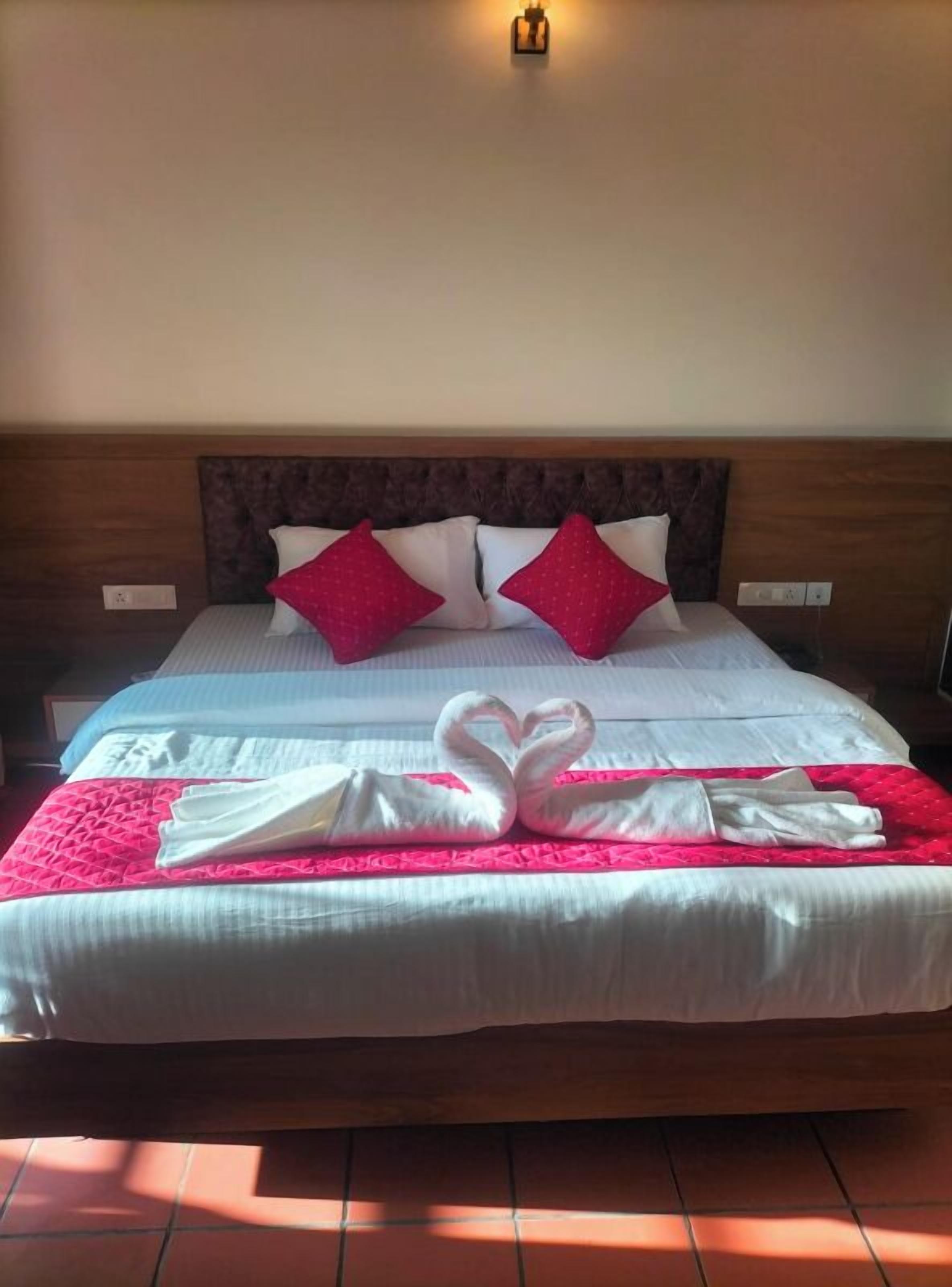 A neatly made bed with a heart-shaped towel arrangement, a wooden headboard, and two red pillows.