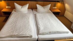 En dobbeltseng med hvide sengetøj og puder, et træhovedgærde, sengeborde med lamper og et natbord med stikkontakt.