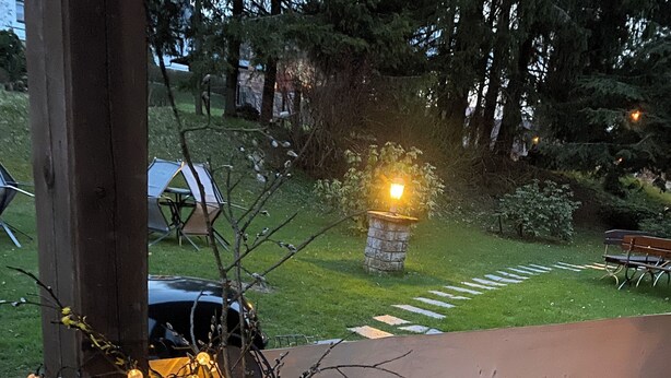 En træbænk med en plantekasse, der indeholder en træskulptur og lys, en stenen lanterne og en belagt sti.