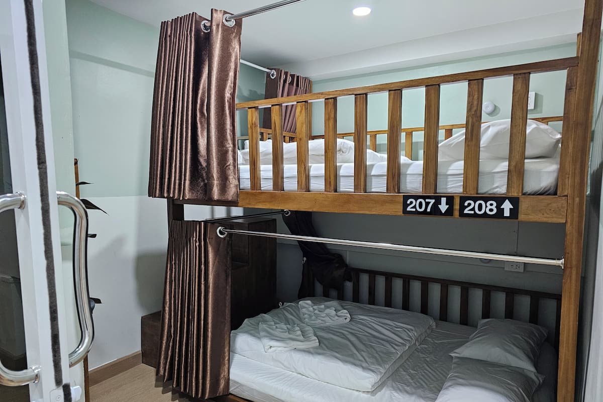 A bunk bed room with a metal railing, a curtain, and a sign indicating room numbers 207 and 208.