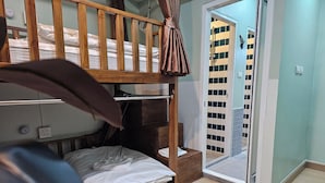 Ein Zimmer mit einem Etagenbett, einem hölzernen Kopfteil, einem kleinen Tisch und einer Tür zu einem gefliesten Bereich.