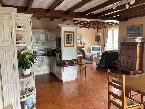 Una cocina amplia con armarios blancos, un comedor con mesa y sillas de madera, y una sala de estar con televisor y asientos cómodos.
