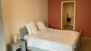 A bedroom with a bed, nightstand, and a door leading to another room.