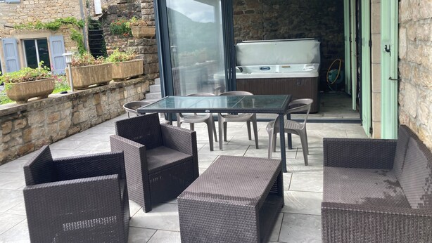 A patio with wicker furniture, a glass table, and a hot tub.