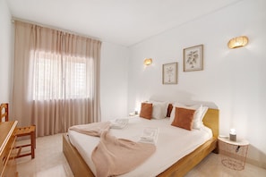 Une chambre bien rangée, avec un lit, des tables de chevet, une chaise et une fenêtre avec des rideaux.