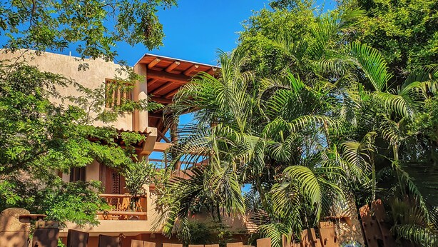 Un edificio tradicional con un balcón de madera, rodeado de exuberante vegetación y palmeras.