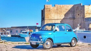 A blue vintage car parked in front of a historic stone building with a flag on top. - GIONI House (Monopoli)