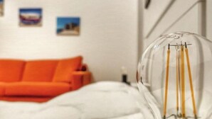 A room with a white bed, an orange couch, and a clear glass bulb with wires. - GIONI House (Monopoli)