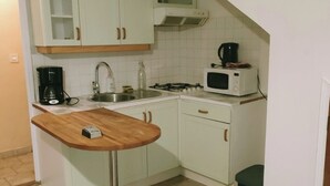 Una cocina pequeña con armarios blancos, una encimera de madera, un microondas, una cafetera y un cubo de basura.