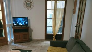Una sala de estar con un sofá, un televisor sobre un mueble bajo, una ventana con cortinas y un adorno en la pared.