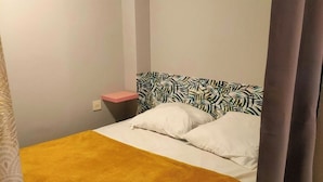 Una cama individual con un cabecero estampado, una mesita de noche y una cortina.