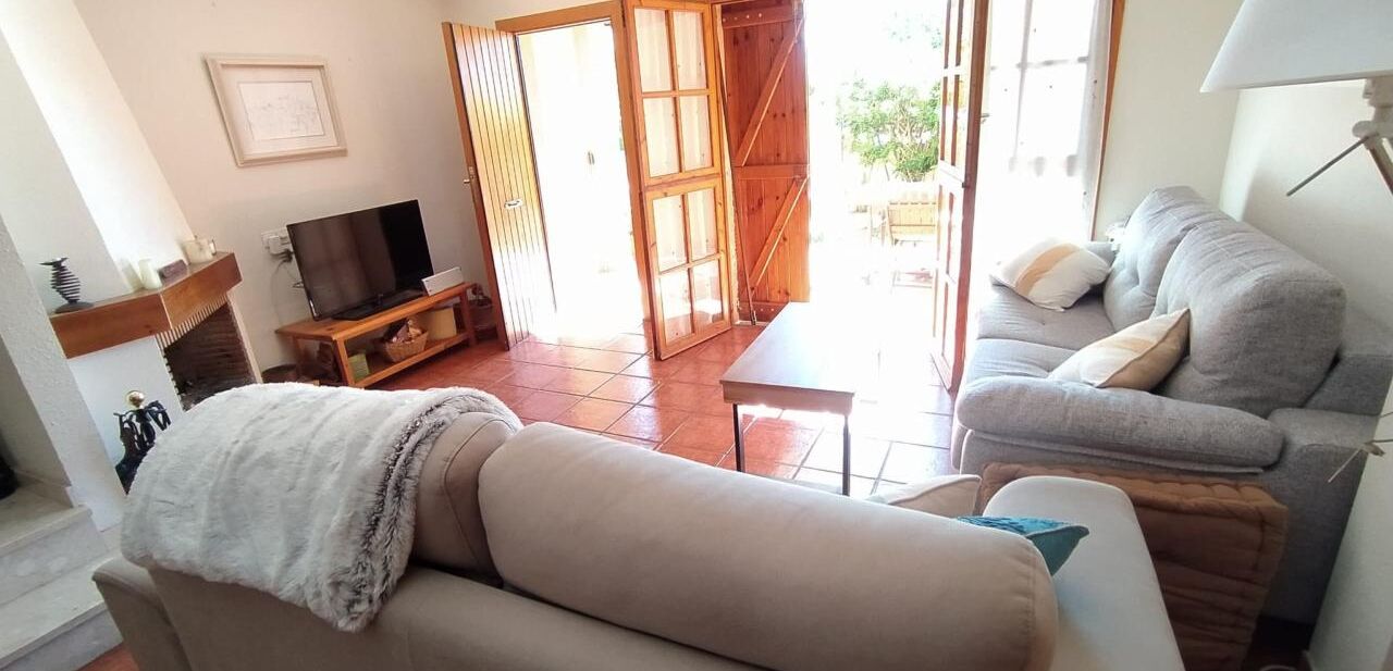 A living room with a sofa, a television, and a table. There is a sliding door leading to an outdoor area.