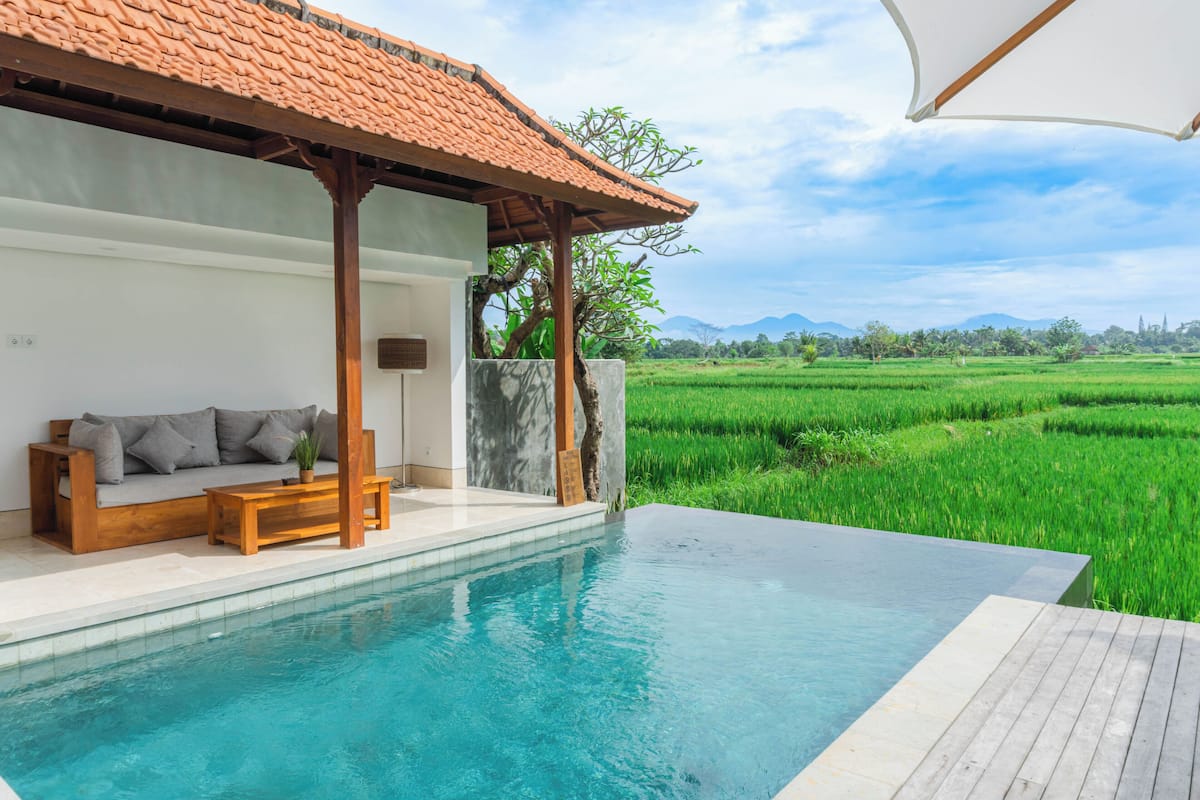 A pool area with a wooden deck, a sofa, and a view of a green field.